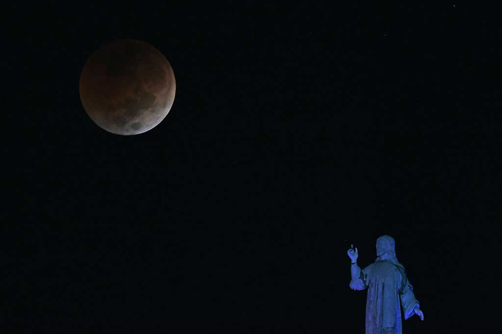 Fenomena blood moon saat gerhana bulan total terlihat melewati monumen Savior of the World di Salvador del Mundo Square, di San Salvador pada Selasa, 8 November 2022. AFP PHOTO/Marvin Recinos