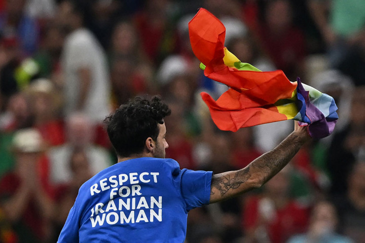 Seorang pria dengan bendera pelangi dan mengenakan T-shirt dengan kata-kata 'Respek untuk Wanita Iran' di punggungnya menyerbu lapangan selama pertandingan di Piala Dunia Qatar, Selasa, 29 November 2022 dini hari WIB.
