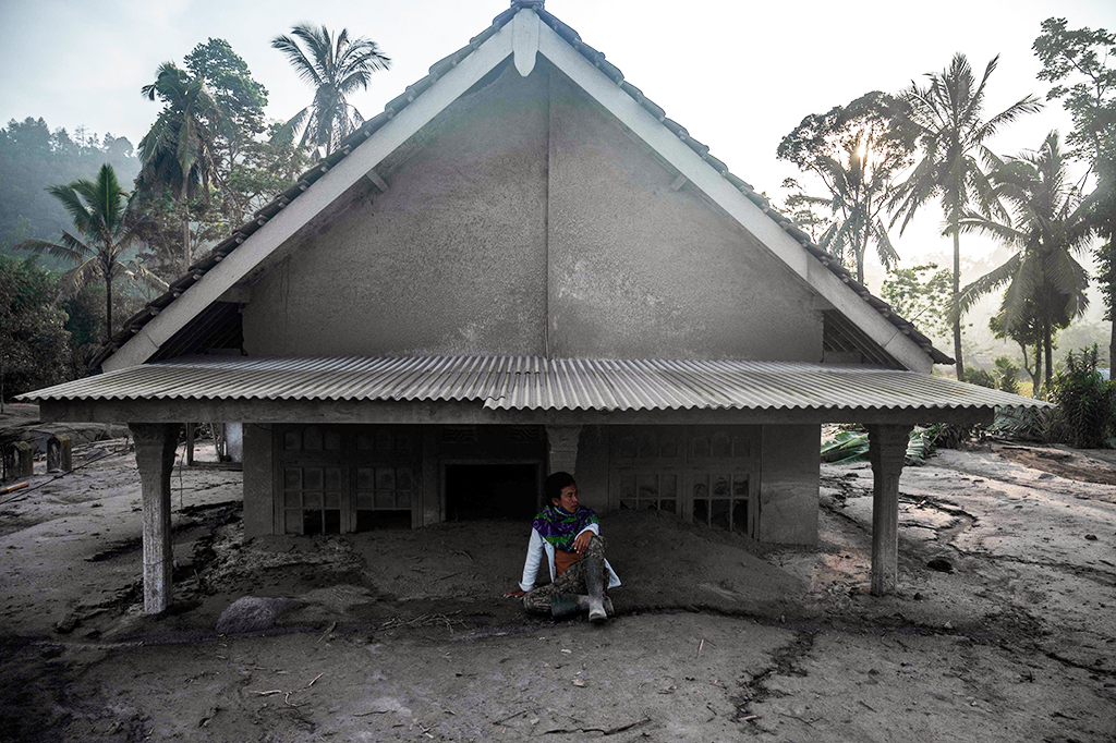 Seorang pria duduk di depan sebuah rumah yang terendam material pasir setelah letusan Gunung Semeru di Dusun Kajar Kuning, Desa Sumberwuluh, Lumajang, Jawa timur, Senin, 5 Desember 2022.