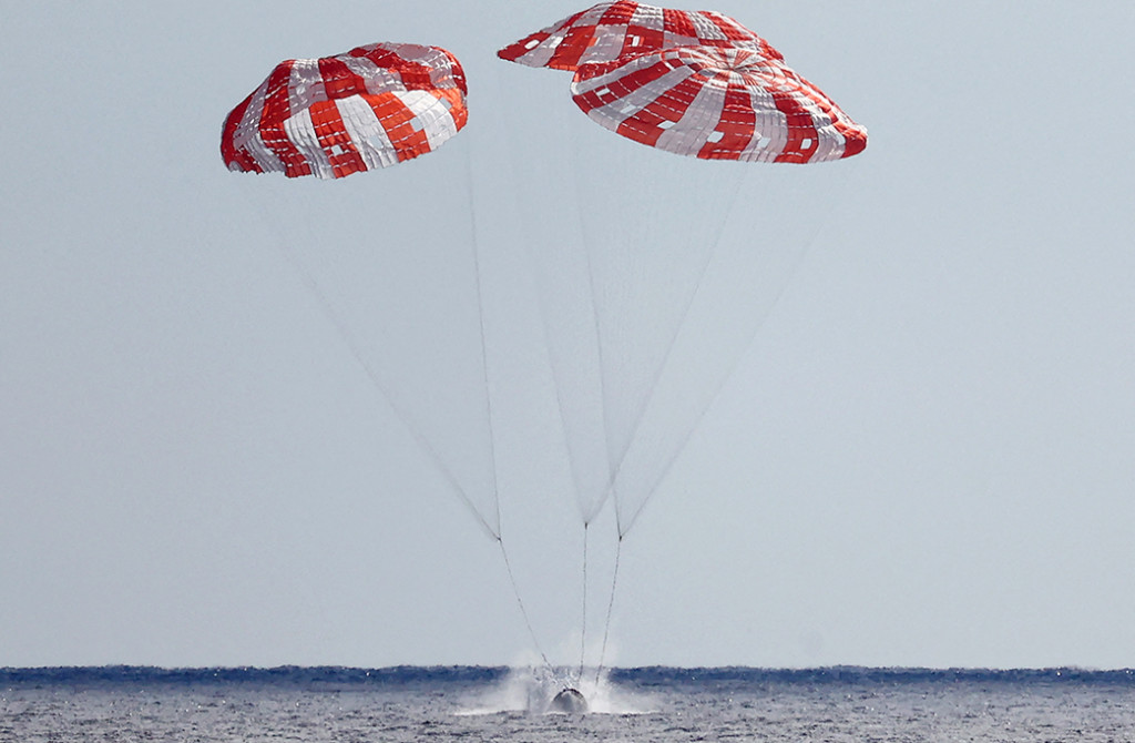Setelah meluncur melalui atmosfer Bumi dengan kecepatan 40.000 kilometer per jam (25.000 mph), kapsul tanpa awak itu melayang ke air dengan bantuan tiga parasut besar berwarna merah dan putih, seperti yang terlihat di NASA TV.