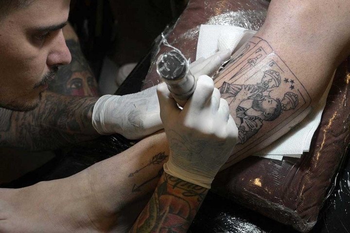 Seorang seniman tato tengah mengerjakan tato penyerang Argentina Lionel Messi mencium trofi Piala Dunia FIFA di kaki seorang pelanggan di Ds Tattoo Shop, Buenos Aires.