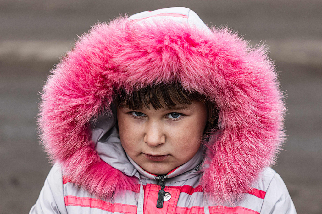 Lisa Shtanko, 8 tahun, berdiri di sisi jalan berlumpur menyaksikan tentara Ukraina lewat, satu dari sedikit anak yang tersisa di kota yang dilanda invasi Rusia.