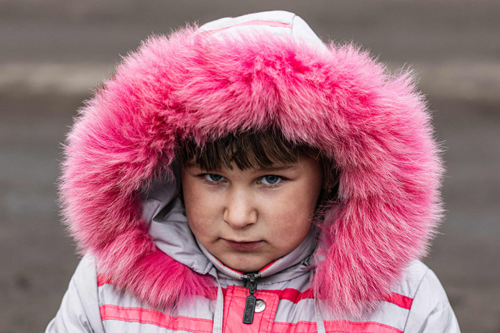 Lisa Shtanko, 8 tahun, berdiri di sisi jalan berlumpur menyaksikan tentara Ukraina lewat, satu dari sedikit anak yang tersisa di kota yang dilanda invasi Rusia.