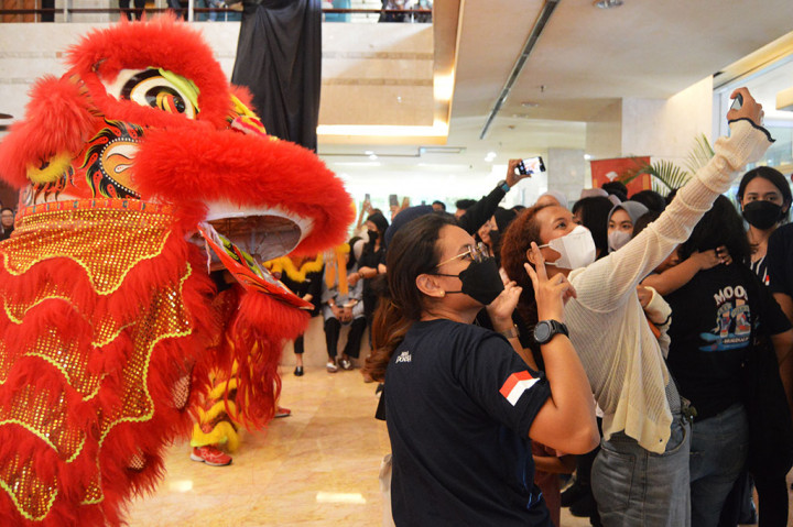 Penonton berfoto selfie dengan latar belakang barongsai.