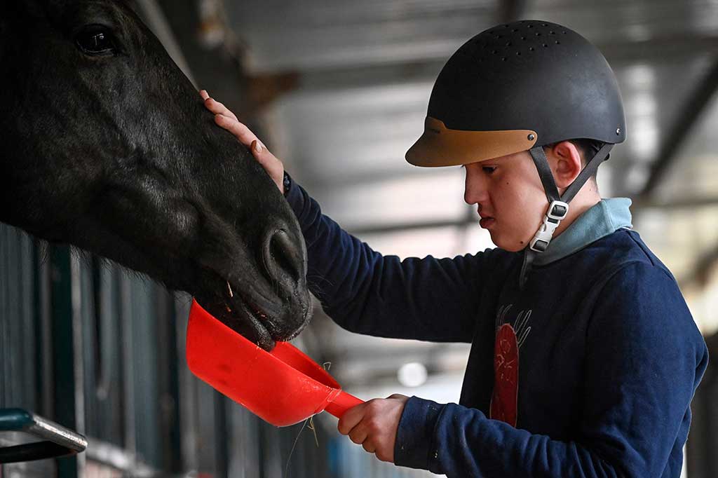 Di sela-sela sesi, yang memiliki pelatih yang membimbing siswa melalui aktivitas menunggang kuda yang disesuaikan, dia juga membantu memberi makan dan merawatnya.