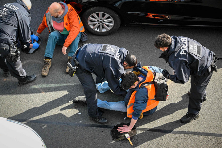Para juru kampanye menghentikan lalu lintas di seluruh kota dengan menempelkan diri mereka ke permukaan jalan, termasuk di jalan raya A100 yang sibuk.