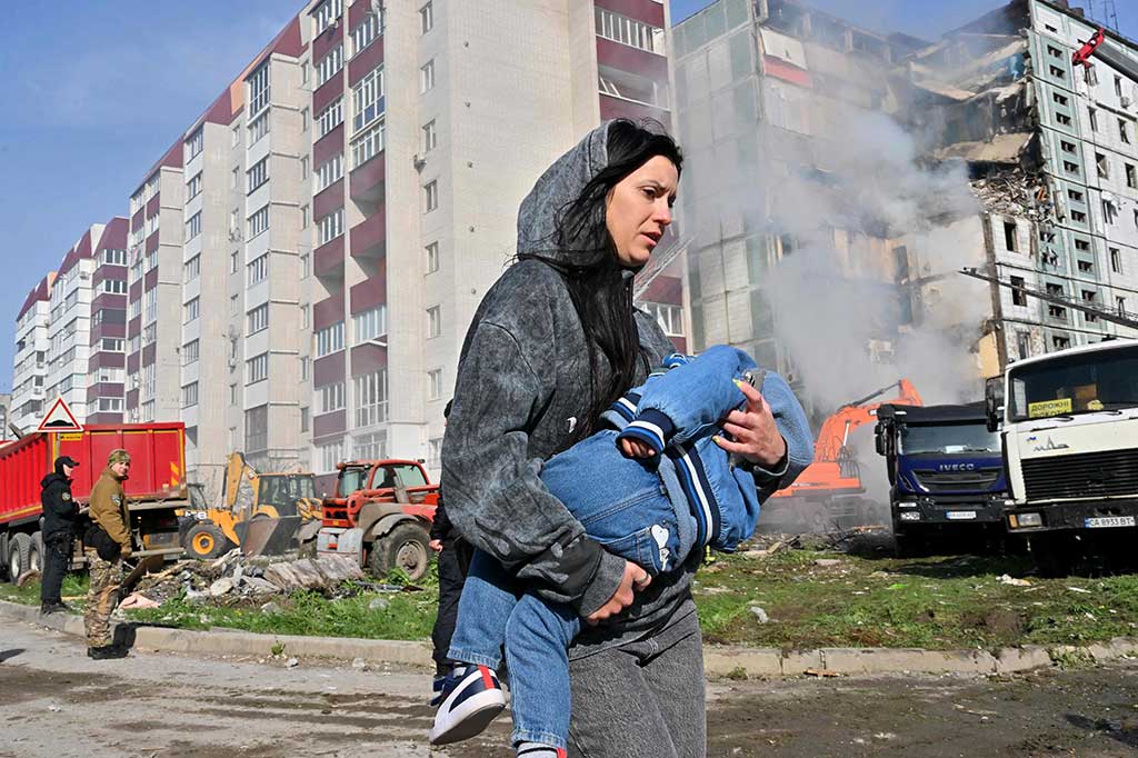 Seorang perempuan berjalan menggendong anak melewati bangunan tempat tinggal yang rusak akibat serangan rudal Rusia di Kyiv, kemarin. Rusia kembali melakukan serangan rudal dan drone yang menargetkan beberapa kota Ukraina dalam semalam.