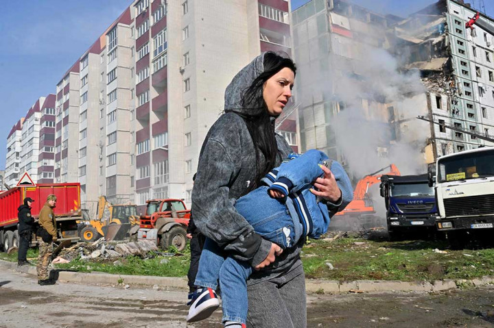 Seorang perempuan berjalan menggendong anak melewati bangunan tempat tinggal yang rusak akibat serangan rudal Rusia di Kyiv, kemarin. Rusia kembali melakukan serangan rudal dan drone yang menargetkan beberapa kota Ukraina dalam semalam.