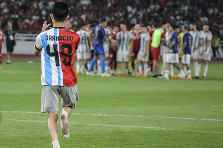 Seorang penonton yang mengenakan jersey belang timnas Argentina dan Indonesia dengan tulisan Garnacho di punggung, berlari ke tengah lapangan sesaat setelah pertandingan usai. 