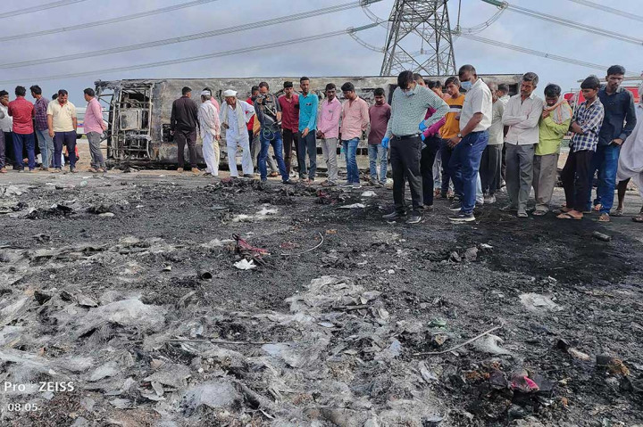 Orang-orang berkumpul di samping sisa-sisa bus (latar belakang) yang terbakar di sepanjang Jalan Tol Samruddhi dekat Sindkhed Raja di distrik Buldhana negara bagian Maharashtra pada Sabtu, 1 Juli 2023. Sedikitnya 25 orang tewas dan delapan lainnya luka-luka setelah sebuah bus terbakar semalam di jalan tol di negara bagian Maharashtra India.