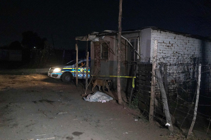 Seekor anjing berada di dekat jenazah yang ditutupi selimut, sekitar 300 meter dari tempat kejadian di mana belasan meninggal akibat kebocoran gas di pemukiman informal Angelo, Boksburg, Afrika Selatan, Kamis, 6 Juli 2023.