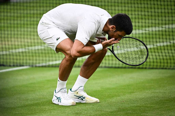 Novak Djokovic dari Serbia mencium rumput saat ia merayakan  keberhasilannya melangkah ke babak final usai meraih kemenangan atas Jannik Sinner pada laga semifinal tunggal putra di Kejuaraan Wimbledon 2023 di The All England Lawn Tennis Club, Wimbledon, London, Jumat, 14 Juli 2023. 
