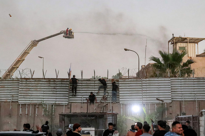 Pendukung ulama Syiah Irak Moqtada al-Sadr memanjat pagar di luar Kedutaan Swedia di Baghdad, saat petugas pemadam kebakaran berusaha memadamkan api di sana, Kamis, 20 Juli 2023.