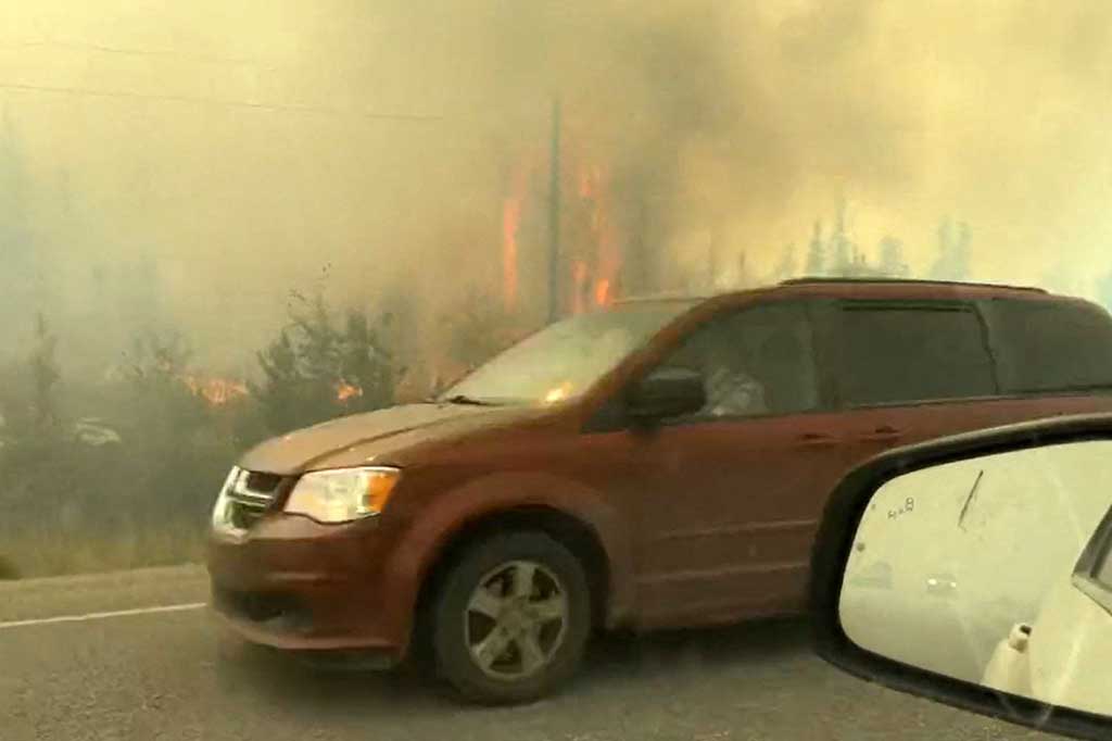 Kendaraan melintas di samping semak belukar yang terbakar di Yellowkife, Wilayah Barat Laut, Kanada, Rabu, 16 Agustus 2023 waktu setempat.