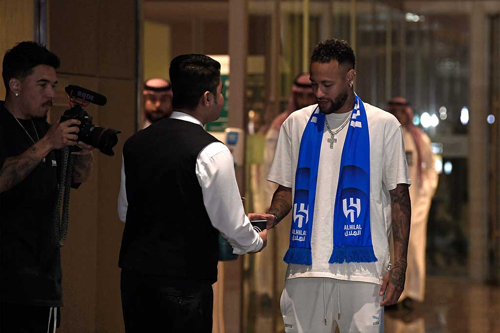 Neymar diterima di ruang tunggu bandara yang dipenuhi oleh pejabat klub dan pers, sebuah salib besar bertabur berlian tergantung di lehernya saat dia berpose untuk difoto.