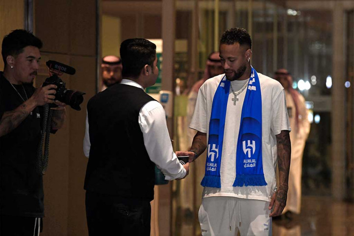 Neymar diterima di ruang tunggu bandara yang dipenuhi oleh pejabat klub dan pers, sebuah salib besar bertabur berlian tergantung di lehernya saat dia berpose untuk difoto.
