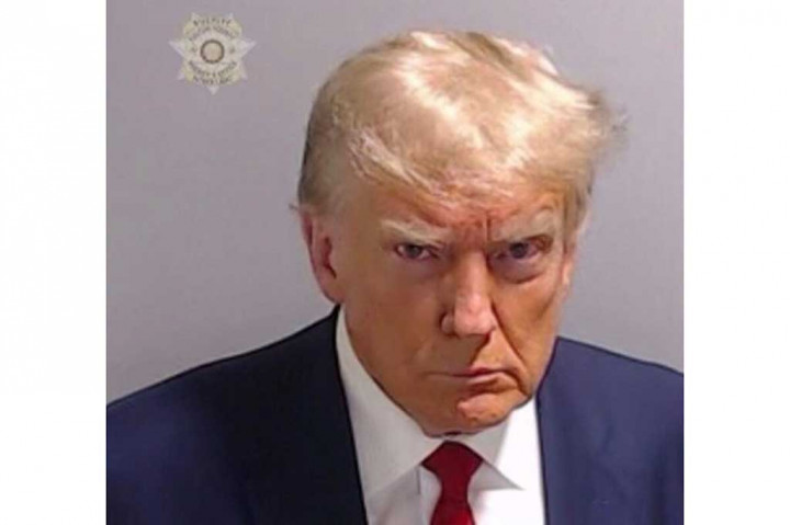 Seperti para terdakwa lain dalam kasus ini yang telah menyerahkan diri sejauh ini, Trump yang berusia 77 tahun juga difoto dan lainnya selama proses pemeriksaan. Dalam foto yang dirilis kantor sheriff, ia yang mengenakan jas biru tua, kemeja putih, dan dasi merah, terlihat merengut ke arah kamera. 