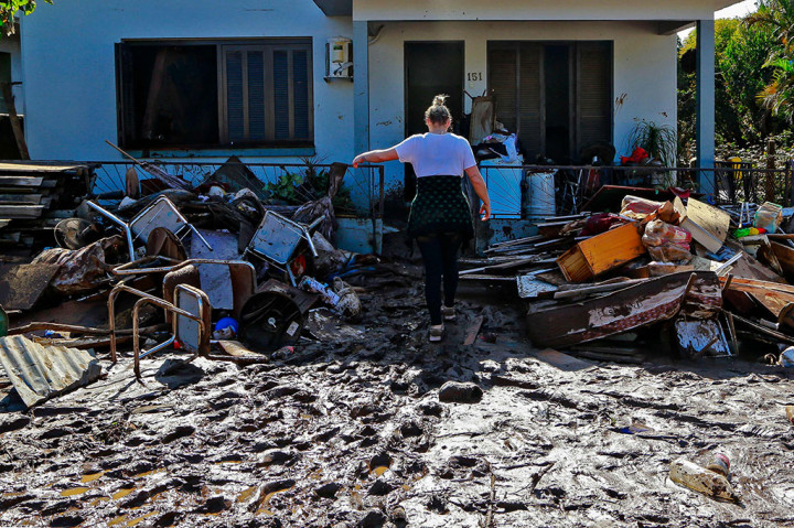 Banjir bandang dan tanah longsor melenyapkan sebagian besar masyarakat yang terkena dampak, meninggalkan bekas rumah yang hancur dan air berwarna coklat berlumpur.