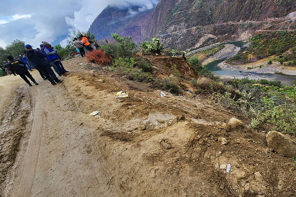 Polisi dan petugas penyelamat menyisir tempat kejadian, sementara orang-orang menyaksikan dari jalan tanah sempit di atas.