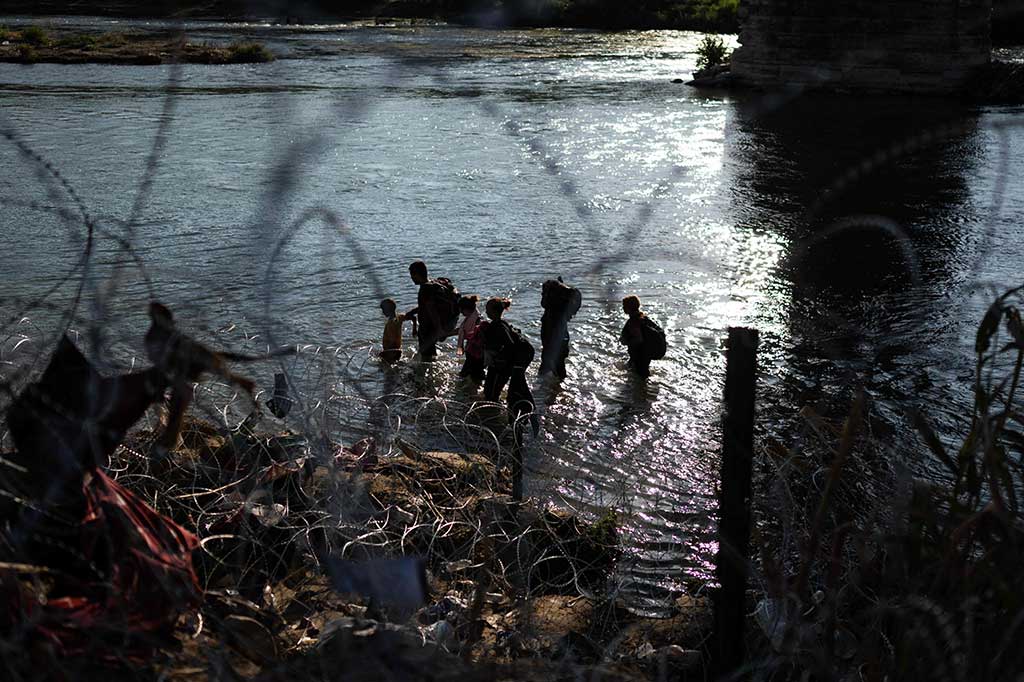 Di wilayah Eagle Pass, para pendatang menyeberangi Sungai Rio Grande untuk mencoba masuk ke wilayah AS, tapi kemudian terhalang oleh pagar kawat berduri.