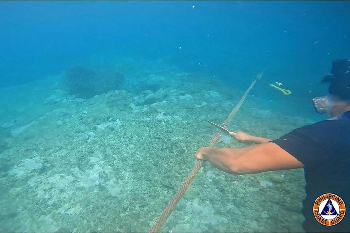 Foto dari Penjaga Pantai Filipina (PCG) menunjukkan personel penjaga pantai memotong tali yang diikatkan pada penghalang terapung yang menghalangi pintu masuk ke Scarborough Shoal di Laut China Selatan yang disengketakan. 