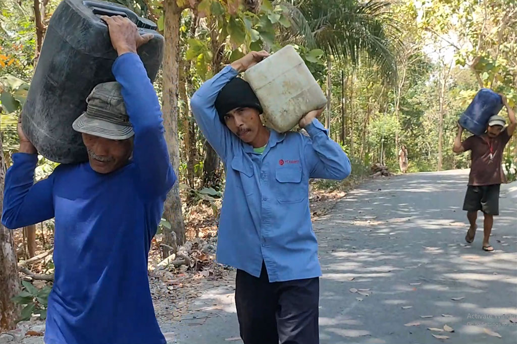 Usai mengisi wadah-wadah yang mereka bawa, upaya warga untuk mendapat air bersih belum selesai. Mereka masih harus membawa pulang air ini dengan berjalan kaki sejauh 1 kilometer.