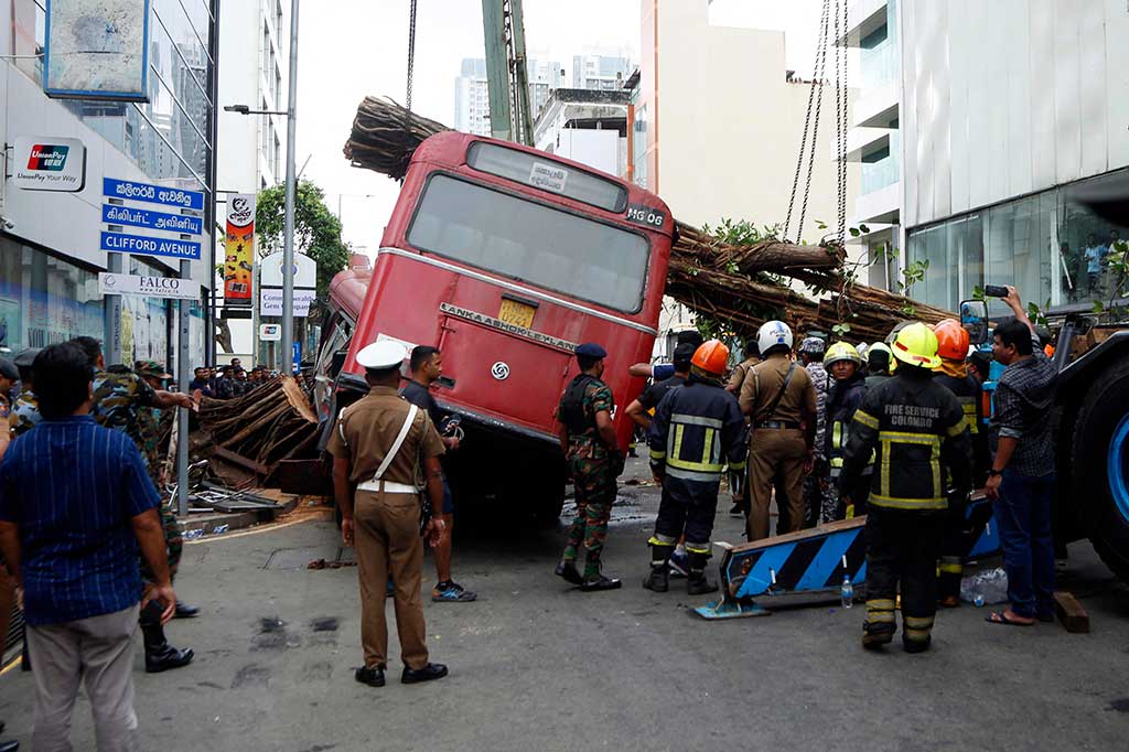 Petugas berjaga-jaga saat pekerja mengevakuasi pohon besar yang tumbang dan menimpa sebuah bus di Kolombo, Sri Lanka, Jumat, 6 Oktober 2023. Sedikitnya lima orang tewas dan beberapa lainnya luka-luka ketika pohon tumbang menimpa bus.
