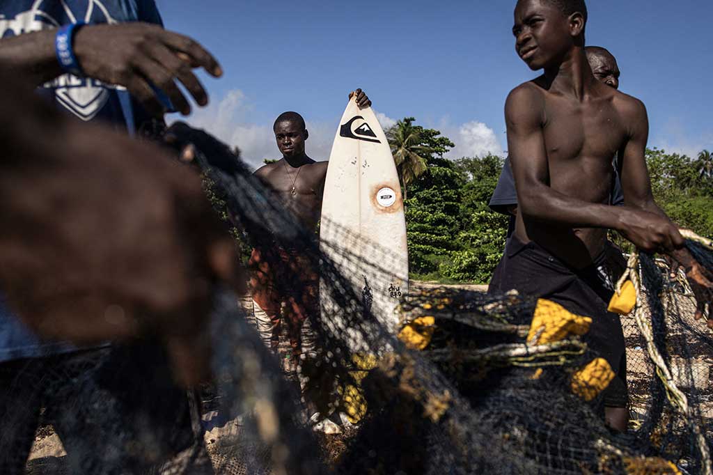 Di belakang mereka, para nelayan berusaha mendorong perahu mereka ke pantai. Nelayan dan peselancar berbagi pantai secara harmonis -- berbaris dalam satu barisan, mereka menarik jaring ikan bersama-sama -- dan beberapa nelayan juga merupakan peselancar.