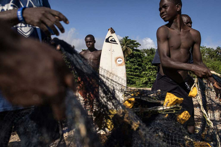 Di belakang mereka, para nelayan berusaha mendorong perahu mereka ke pantai. Nelayan dan peselancar berbagi pantai secara harmonis -- berbaris dalam satu barisan, mereka menarik jaring ikan bersama-sama -- dan beberapa nelayan juga merupakan peselancar.