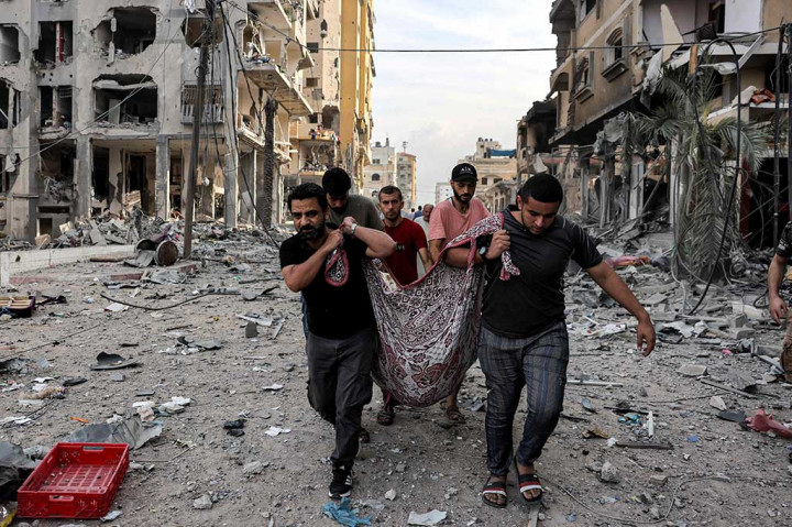 Pria Palestina membawa jenazah seseorang yang tewas akibat pemboman Israel di sepanjang jalan yang dipenuhi puing-puing di distrik al-Karama di Kota Gaza, Rabu, 11 Oktober 2023, di hari kelima pertempuran sengit antara gerakan Islam Palestina Hamas dan Israel.