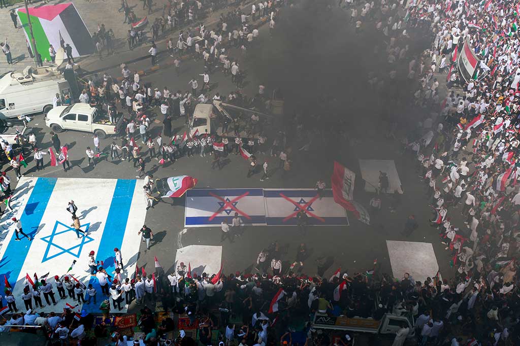 Para pengunjuk rasa mengibarkan bendera Palestina dan Irak, sementara sebuah bendera Israel berukuran besar dikibarkan di tanah untuk diinjak-injak oleh para demonstran.