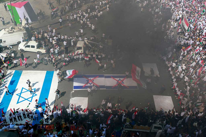 Para pengunjuk rasa mengibarkan bendera Palestina dan Irak, sementara sebuah bendera Israel berukuran besar dikibarkan di tanah untuk diinjak-injak oleh para demonstran.