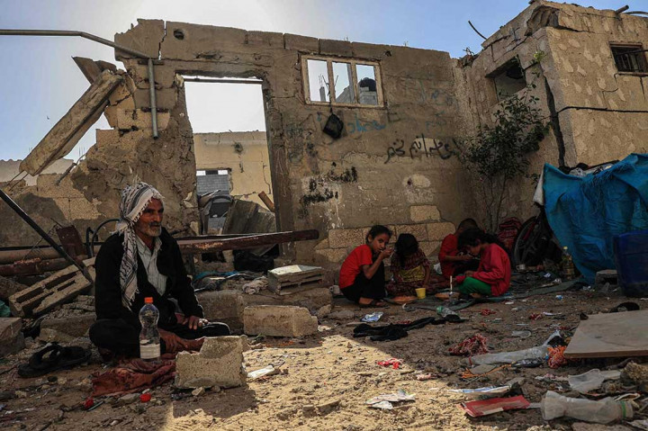 Anak-anak terdampak agresi serangan Israel menyantap makanan mereka, sementara ayahnya, Salman, menyaksikan mereka di tengah reruntuhan rumah keluarga yang hancur akibat serangan Israel di Rafah, Jalur Gaza, Selasa, 7 November 2023.