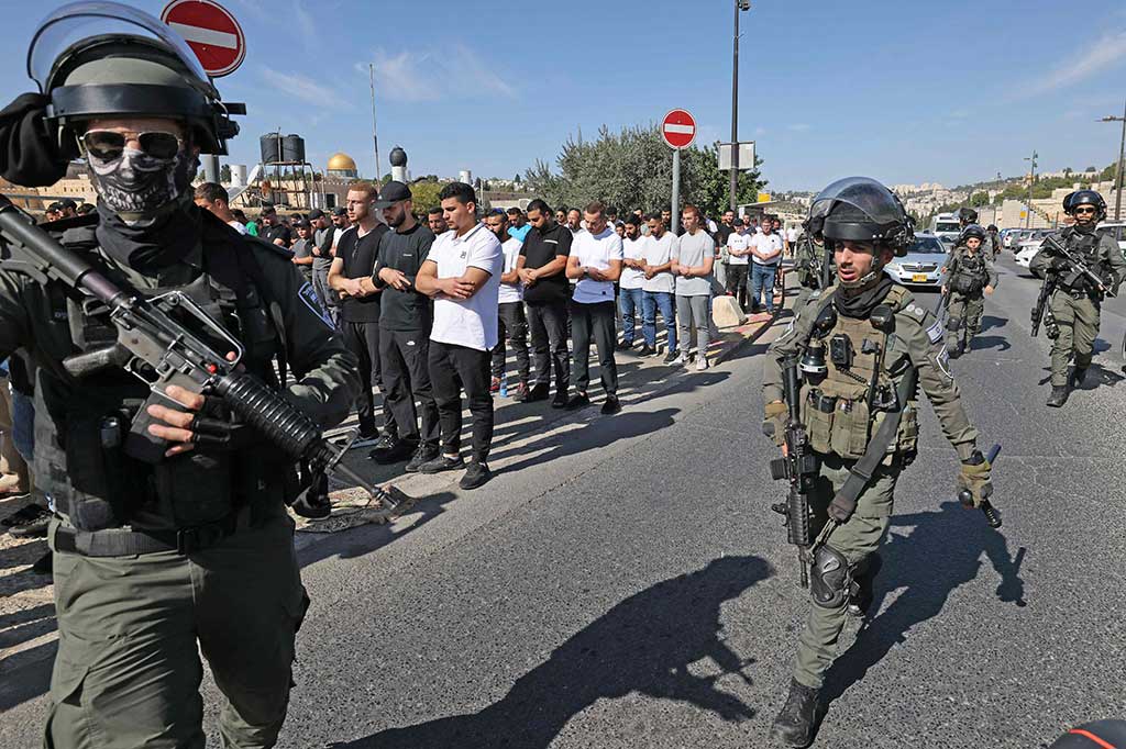 Pasukan keamanan Israel berjalan melewati warga Muslim Palestina yang melaksanakan salat Jumat di lingkungan Ras al-Amud di Yerusalem Timur, pada 10 November 2023, menyusul pembatasan usia oleh keamanan Israel hingga di atas 50 tahun bagi jemaah yang ingin mengaksesnya.