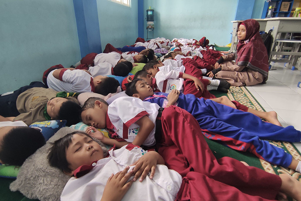 Jam dinding menunjukkan pukul 13.30 WIB, puluhan siswa terlihat tidur berhimpitan di ruang kelas 1 B SD Muhammadiyah 4 Zam-zam Desa Jumputrejo Kecamatan Sukodono Kabupaten Sidoarjo, Senin, 4 Desember 2023. Sementara lantunan murottal atau ayat-ayat suci Alquran samar-samar terdengar.