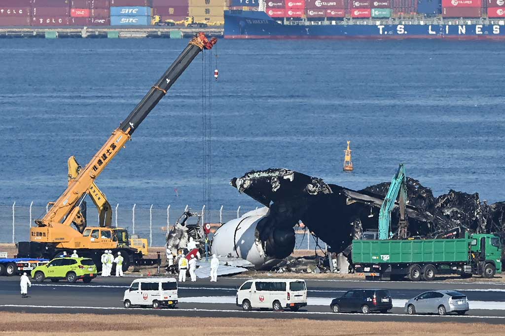 Puing-puing pesawat penumpang Japan Airlines (JAL) dibersihkan dari area landasaan pacu Bandara Internasional Tokyo, di Haneda, Jumat, 5 Januari 2024.