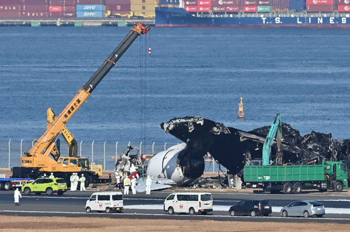 Puing-puing pesawat penumpang Japan Airlines (JAL) dibersihkan dari area landasaan pacu Bandara Internasional Tokyo, di Haneda, Jumat, 5 Januari 2024.