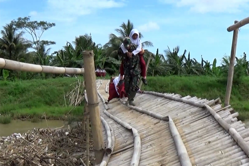 Untuk menyeberang, para siswa harus berpegangan kuat pada lantai jembatan, bahkan ada yang terpaksa digendong oleh anggota Babinsa yang bertugas di desa tersebut.