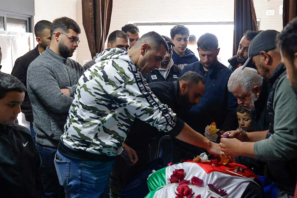 Para pelayat meletakkan bunga di tubuh Tawfeek Ajaq, remaja Palestina berkewarganegaraan AS yang terbungkus bendera, setelah ia ditembak mati sehari sebelumnya di Tepi Barat, menjelang prosesi pemakamannya di Desa Silwad, pada 20 Januari 2024. 