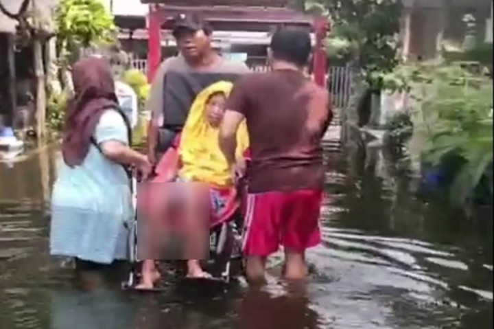 Ada seorang ibu lansia yang terpaksa dievakuasi warga ke tempat aman. Ibu tersebut dievakuasi masih duduk di kursi rodanya.