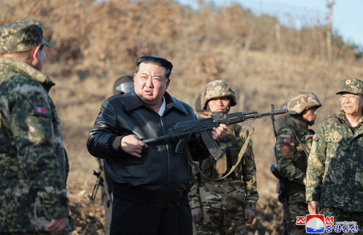 Mengenakan jaket kulit hitam, Kim Jong Un terlihat berbicara dengan barisan tentara bersenjata lengkap dalam kamuflase, mengawasi latihan penembakan dan memeriksa persenjataan.