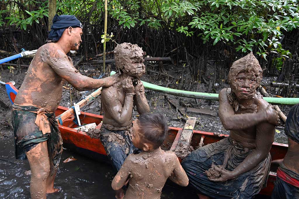 Warga melumurkan lumpur kepada seorang anak saat mengikuti tradisi Mebuug-buugan di kawasan Kedonganan, Badung, Bali, Selasa, 12 Maret 2024.