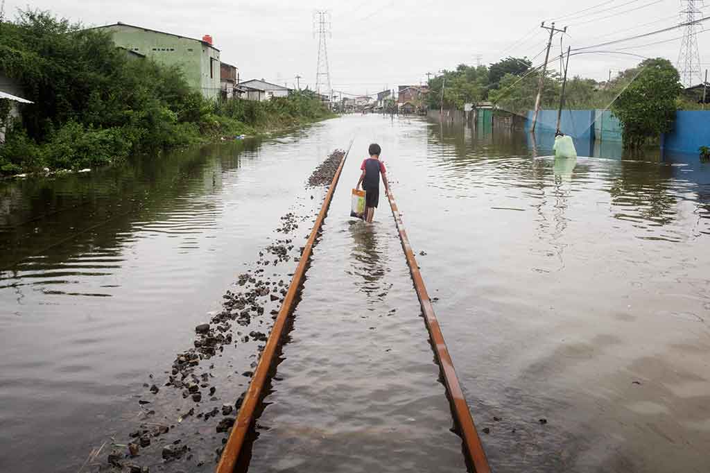 Seorang anak laki-laki berjalan di tengah rel kereta api yang tergenang banjir usai hujan deras melanda Semarang, Jawa Tengah, pada Jumat, 15 Maret 2024.
