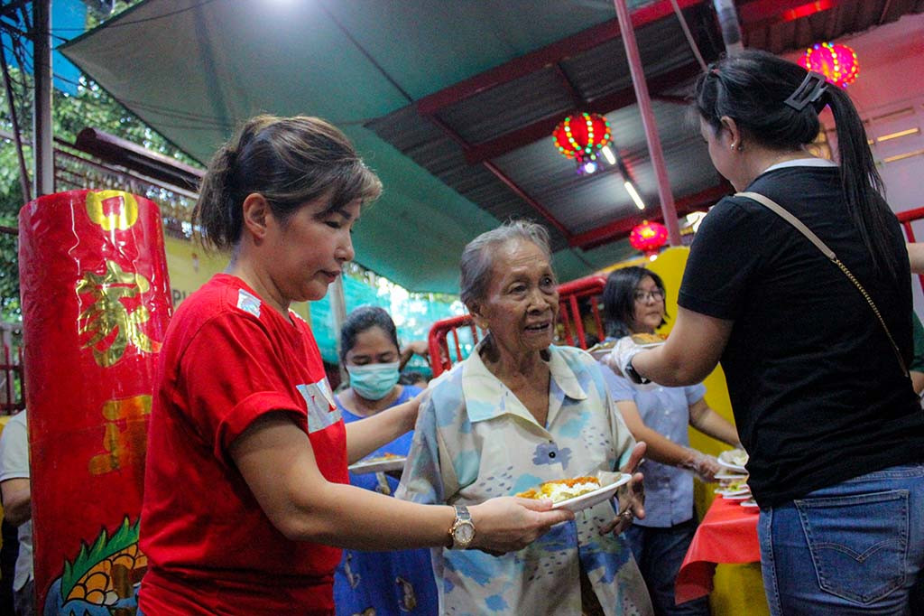 Sejumlah petugas pun sibuk menyiapkan makanan dan minuman di atas meja panjang yang nantinya akan dibagikan kepada warga yang telah mengantre di dalam wihara.