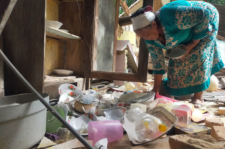 Nenek Nanik memungut piring dan gelas yang masih bisa diselamatkan dari rumahnya yang rusak akibat diguncang gempa.