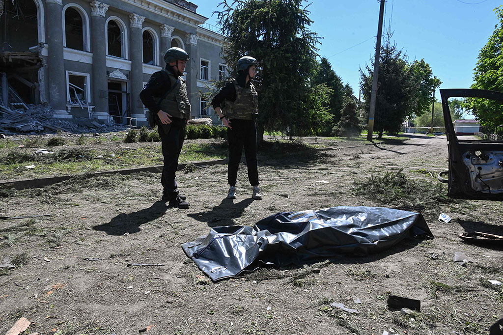 Petugas polisi Ukraina berdiri di samping jenazah yang berada di dalam kantong jenazah setelah serangan Rusia di Desa Zolochiv, wilayah Kharkiv, Ukraina, Rabu, 1 Mei 2024.
