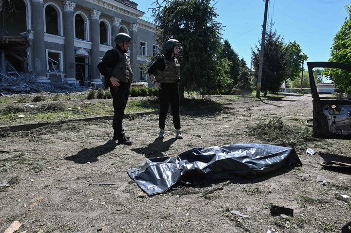 Petugas polisi Ukraina berdiri di samping jenazah yang berada di dalam kantong jenazah setelah serangan Rusia di Desa Zolochiv, wilayah Kharkiv, Ukraina, Rabu, 1 Mei 2024.