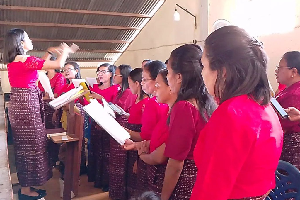 Tampak Dengan Baju atas merah, para anggota koor bernyanyi dengan semangat mengiringi suasana Ibadah misa selama kurang lebih 3 jam di Gereja Santo Markus Waimana satu.