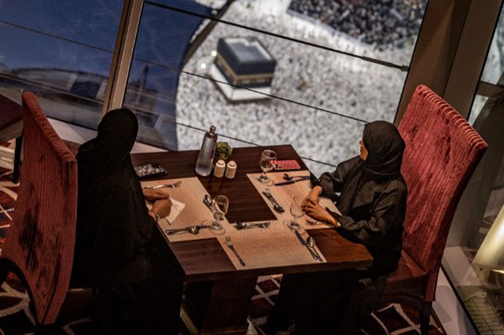 Dua perempuan duduk di sebuah restoran saat umat Muslim berjalan mengelilingi Ka'bah (tawaf), di Masjidil Haram, Mekah, Arab Saudi, Kamis, 13 Juni 2024, menjelang pelaksanaan ibadah haji.