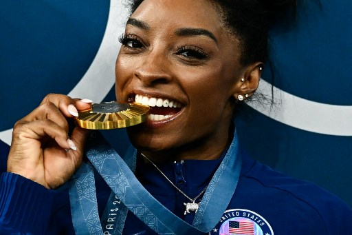 Medali emas Olimpiade keenam Simone Biles tergantung di leher, begitu pula seekor kambing kecil yang berkelap-kelip, sebagai pengingat bagi dirinya yang dipuji sebagai pesenam terhebat sepanjang masa (the greatest of all time atau GOAT).